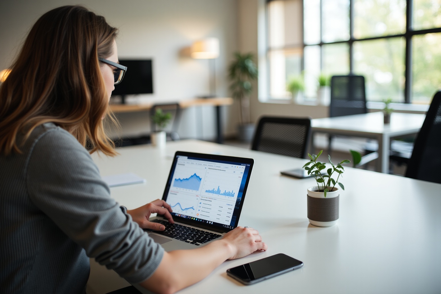 Woman working on laptop, analyzing data, office environment.