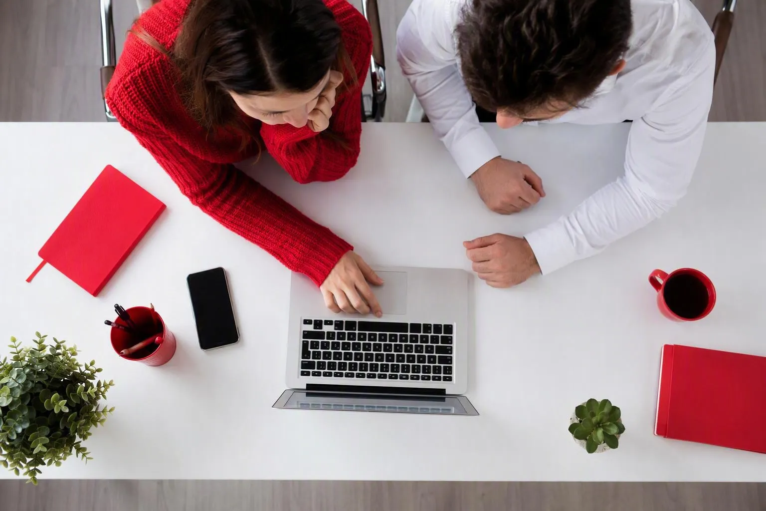Two people working together at a desk with laptops and coffee.