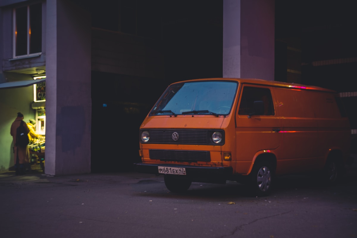 Fourgonnette Volkswagen orange garée dans une rue sombre.