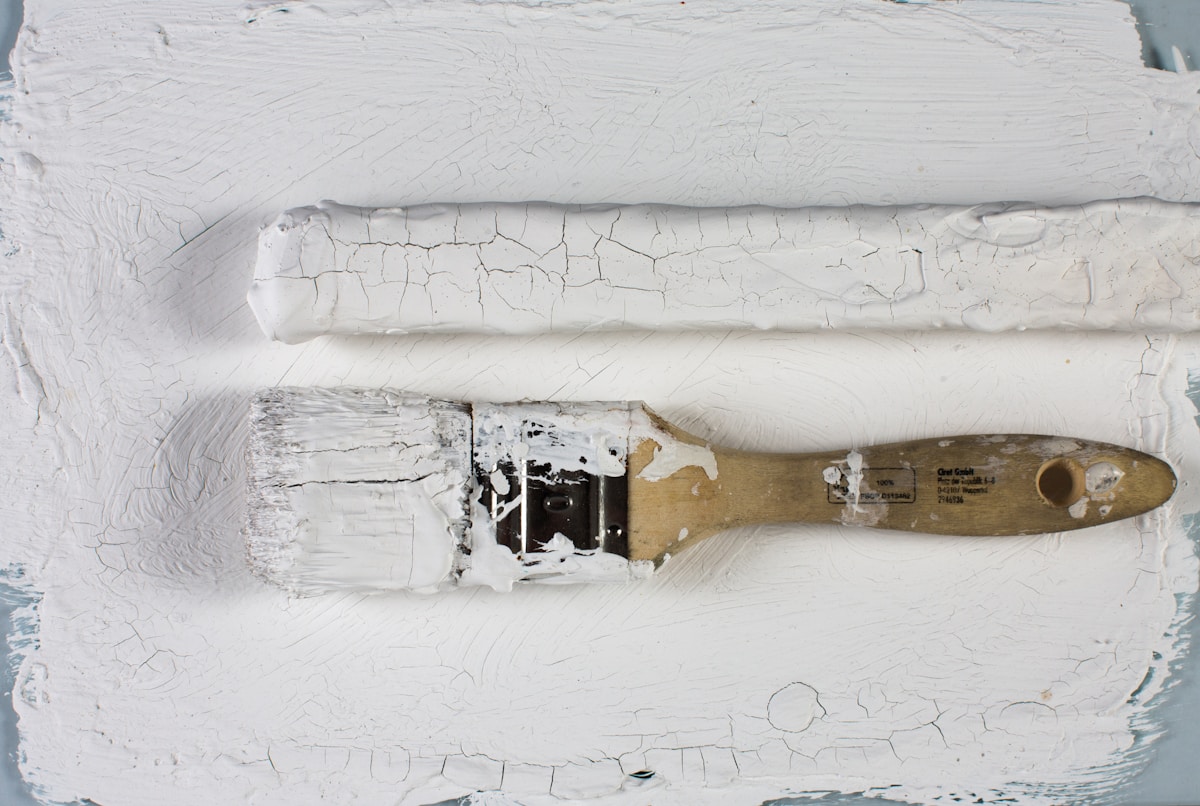 Pinceau à peinture usagé sur surface craquelée blanche.