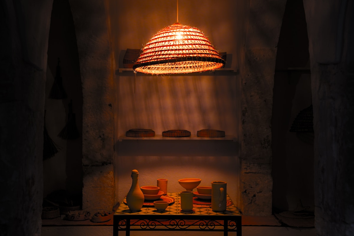 Woven lamp illuminates rustic display shelf with pottery.