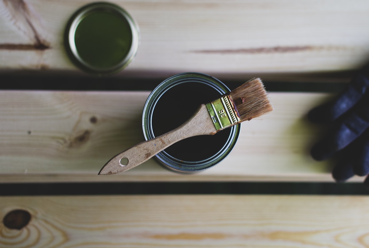 Pots de peinture verts et pinceau sur une surface en bois.