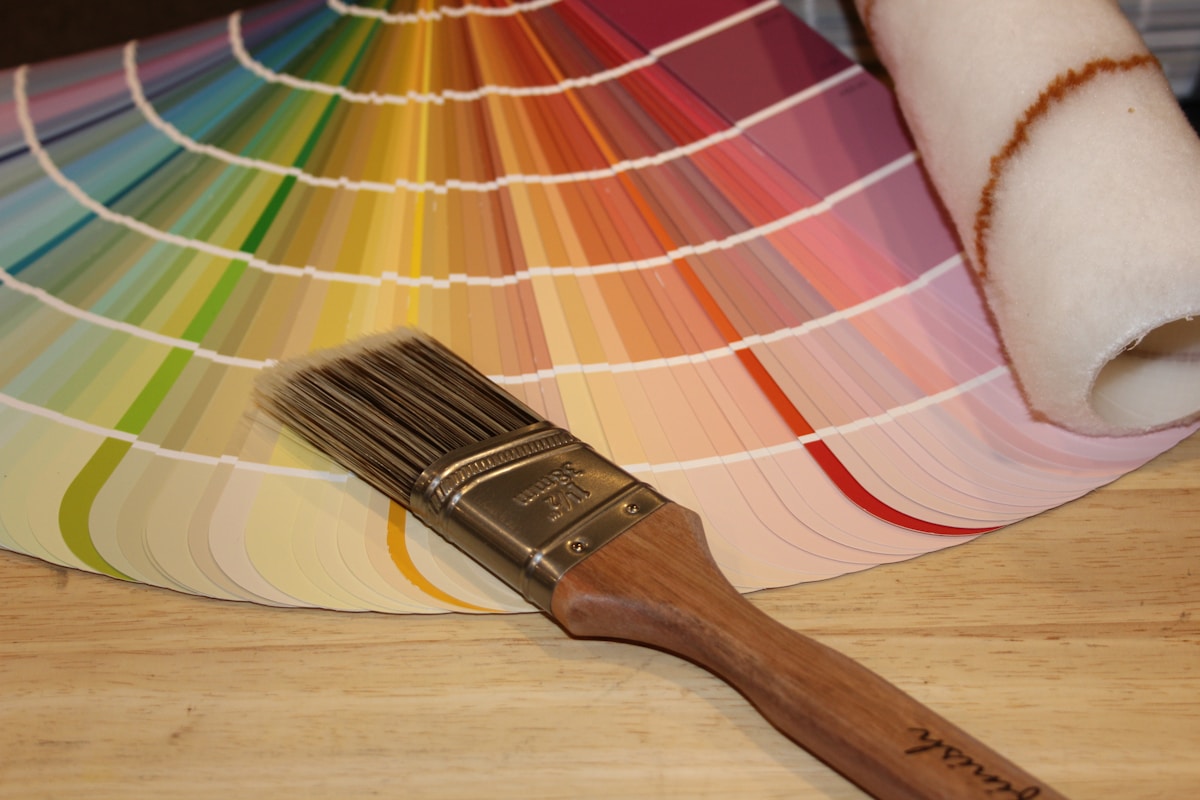 Palette de couleurs, pinceau et rouleau de papier peint sur une surface en bois.