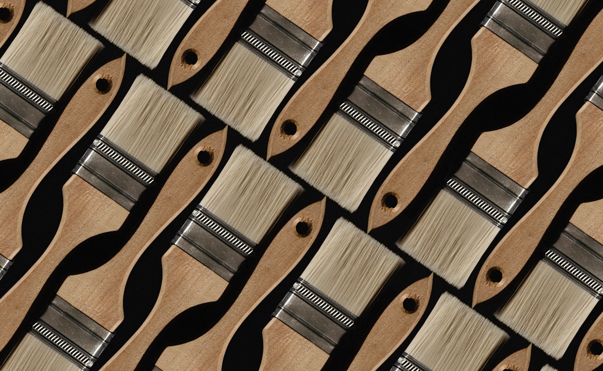 Pinceaux de peinture en bois et métal alignés de manière répétitive.