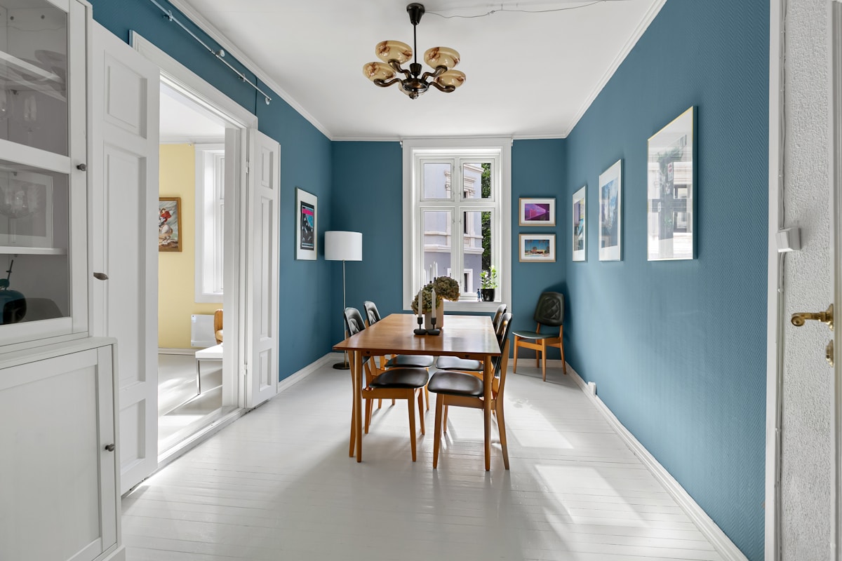 Salle à manger lumineuse avec murs bleus, mobilier en bois et luminaire doré.