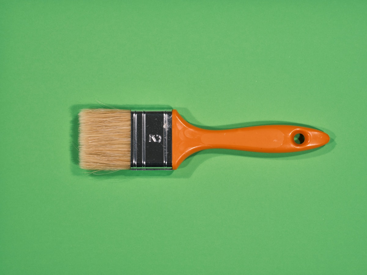 Pinceau orange avec poils naturels sur fond vert.