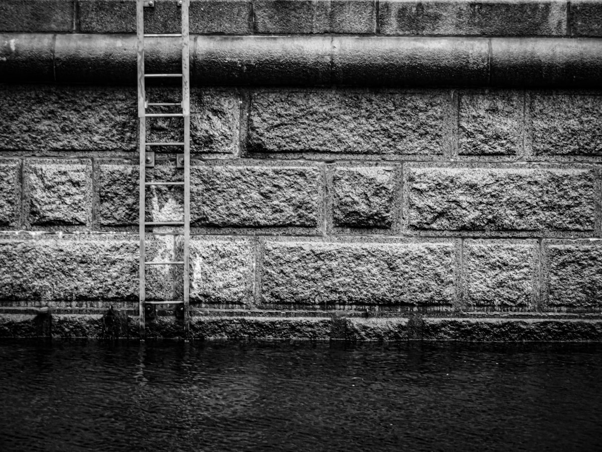 Mur de pierre, échelle, reflet dans l'eau, contraste sombre.