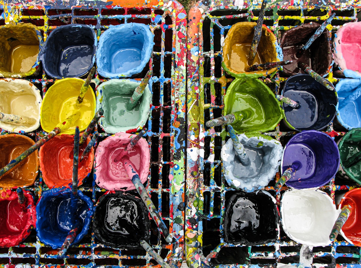 Palette de couleurs vives et variées, pots de peinture, pinceaux, créativité artistique.