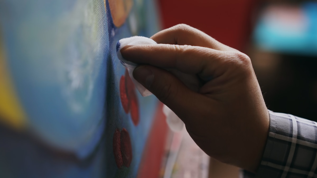 Close-up of a hand adding detail to a colorful painting.