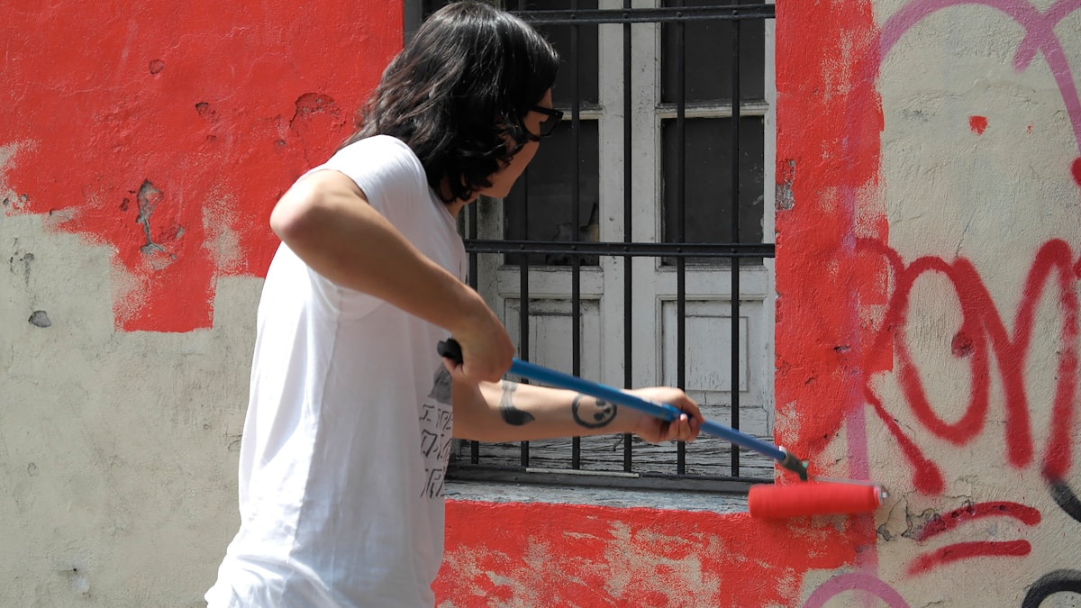 Personne peignant un mur rouge avec un rouleau de peinture.