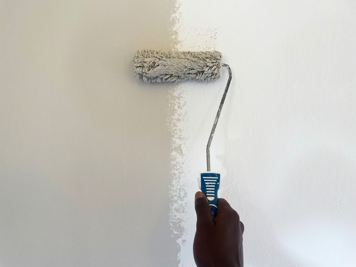 Rouleau de peinture appliquant un enduit blanc sur un mur.