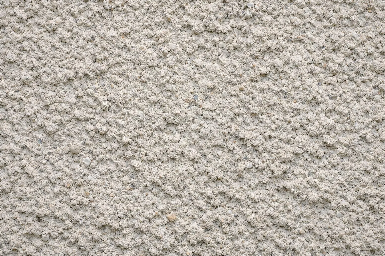 Gros plan du mur extérieur montrant la texture détaillée du crépi avec une surface granuleuse rugueuse, des particules d'agrégat visibles et une patine naturelle dans des tons neutres, photographié à la lumière du jour.