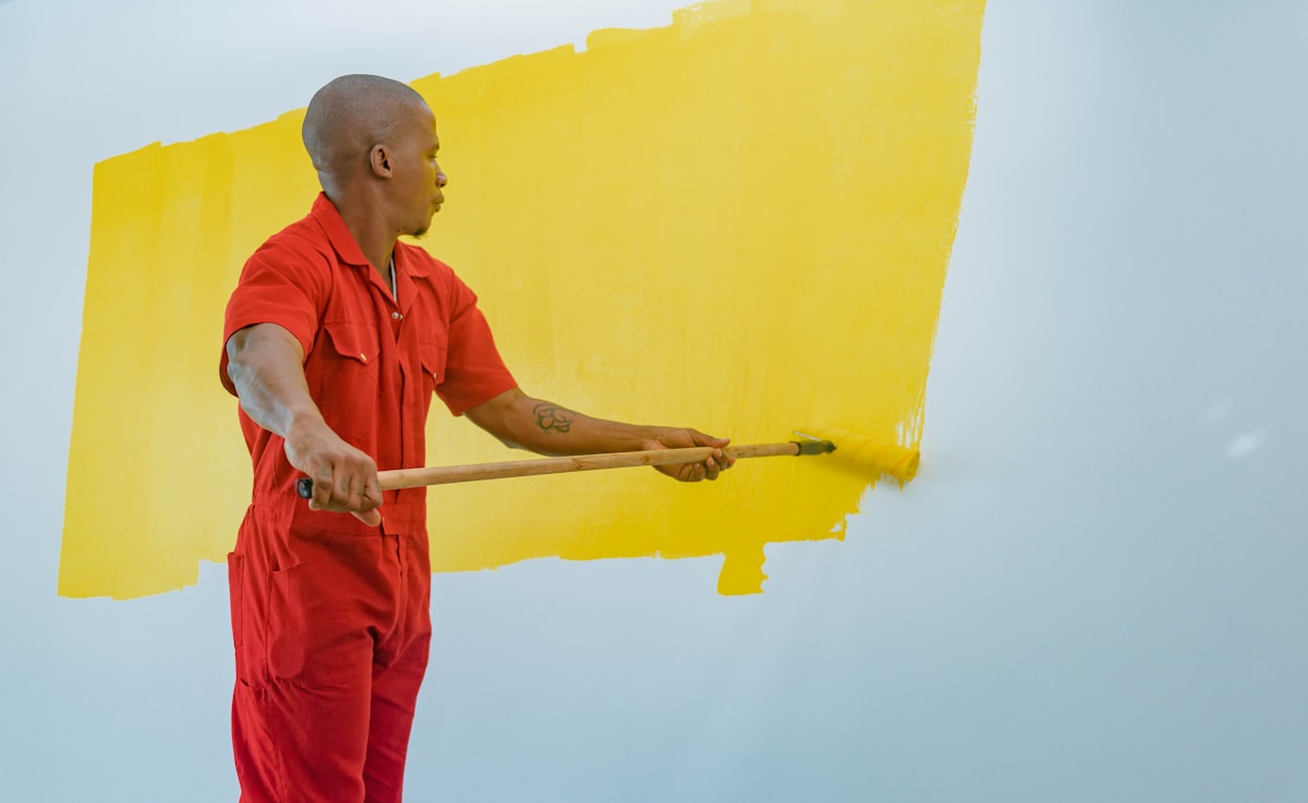 Un homme en combinaison rouge peignant un mur jaune.