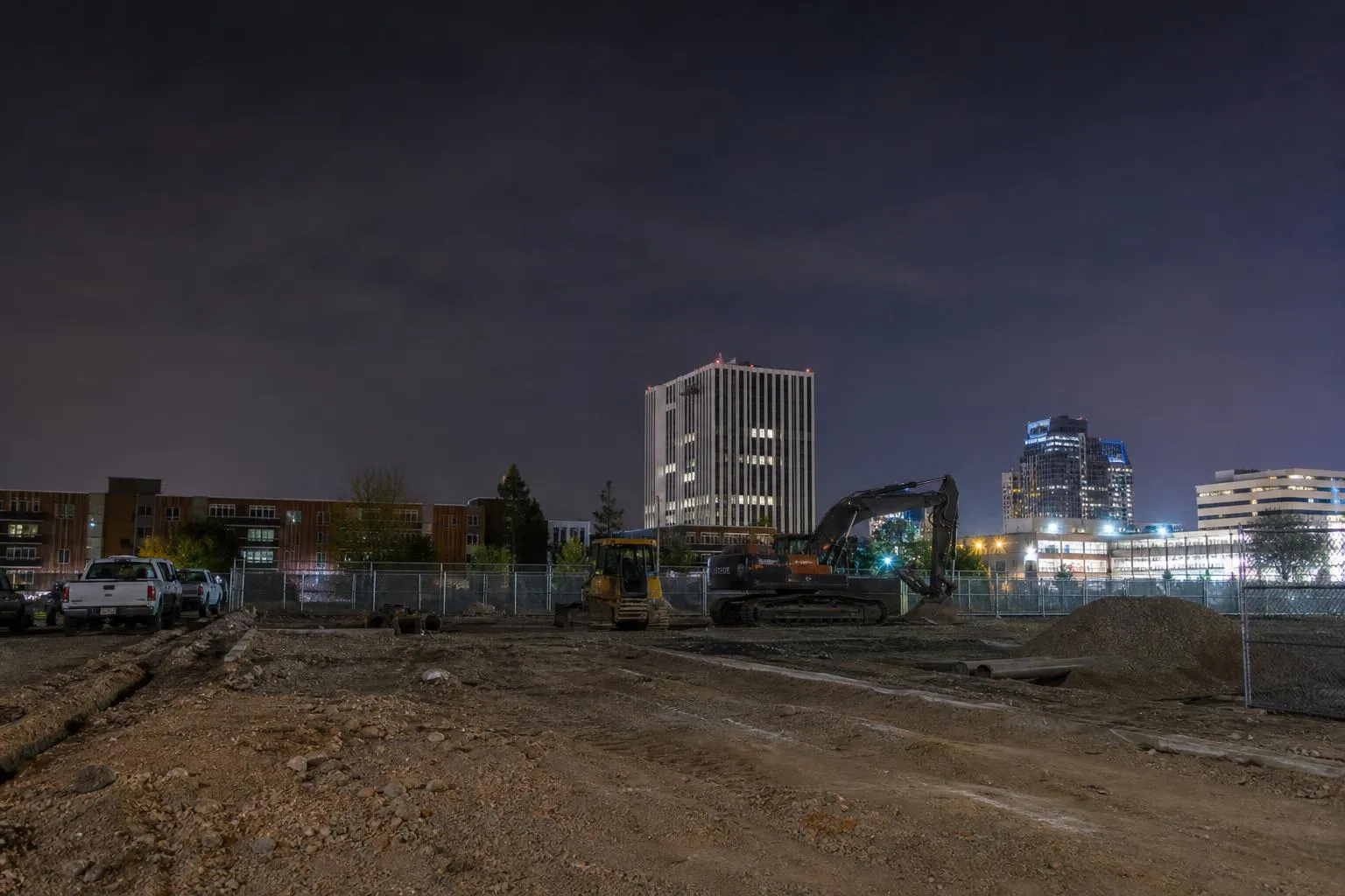 Nighttime cityscape with construction site and excavator equipment.