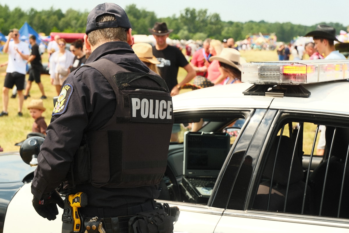 Police officer stands by patrol car at outdoor event.