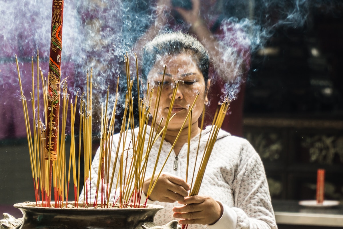 Femme âgée brûlant des bâtons d'encens dans un temple.