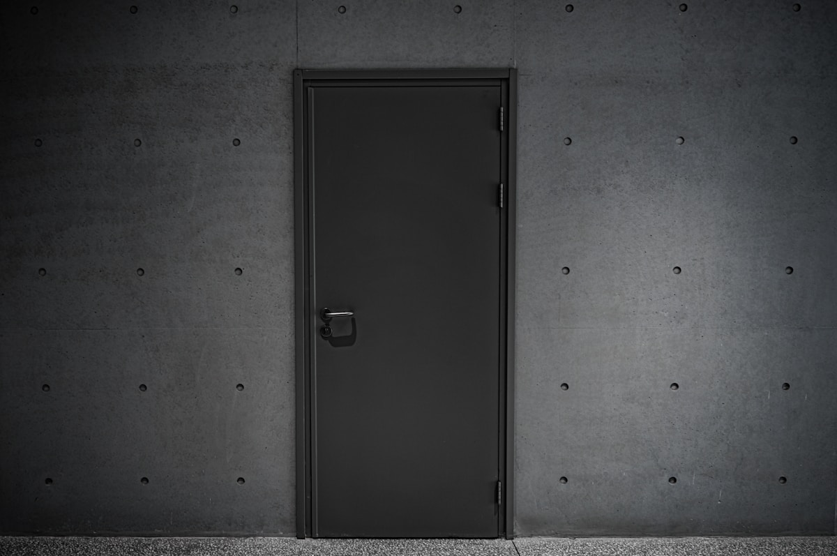 Porte noire dans un mur de béton gris.