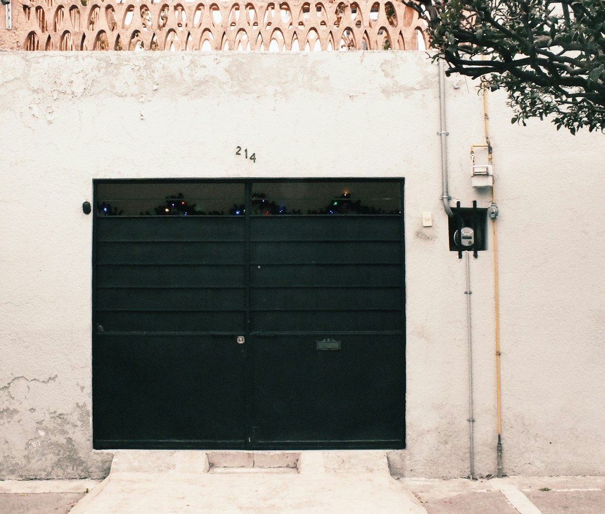 Porte de garage noire avec numéro 214, mur blanc orné de motifs, lampadaire.
