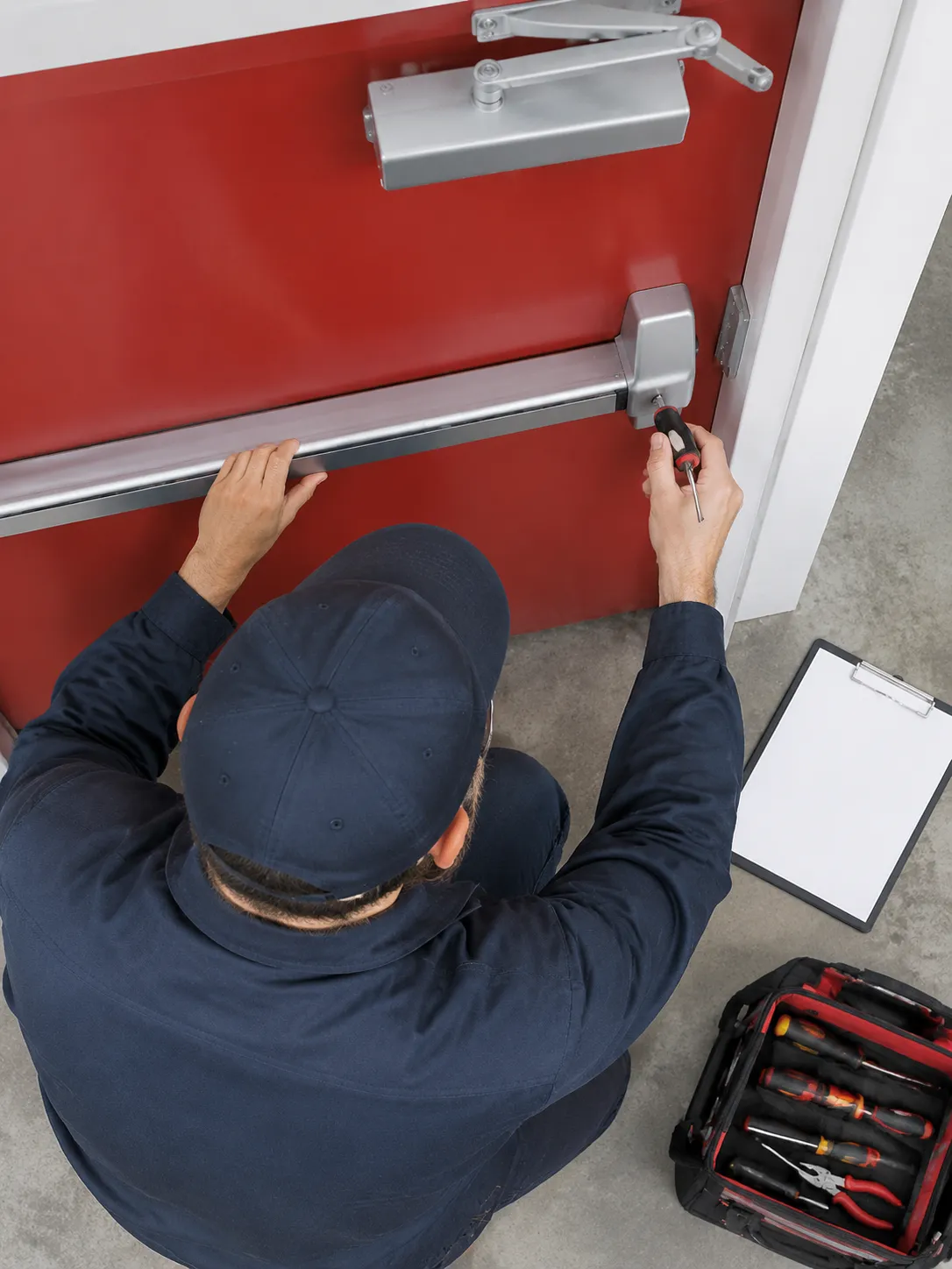 Technicien réparant une barre antipanique sur une porte rouge