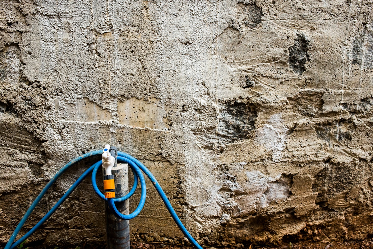 Tuyau d'arrosage bleu sur un mur de béton texturé.
