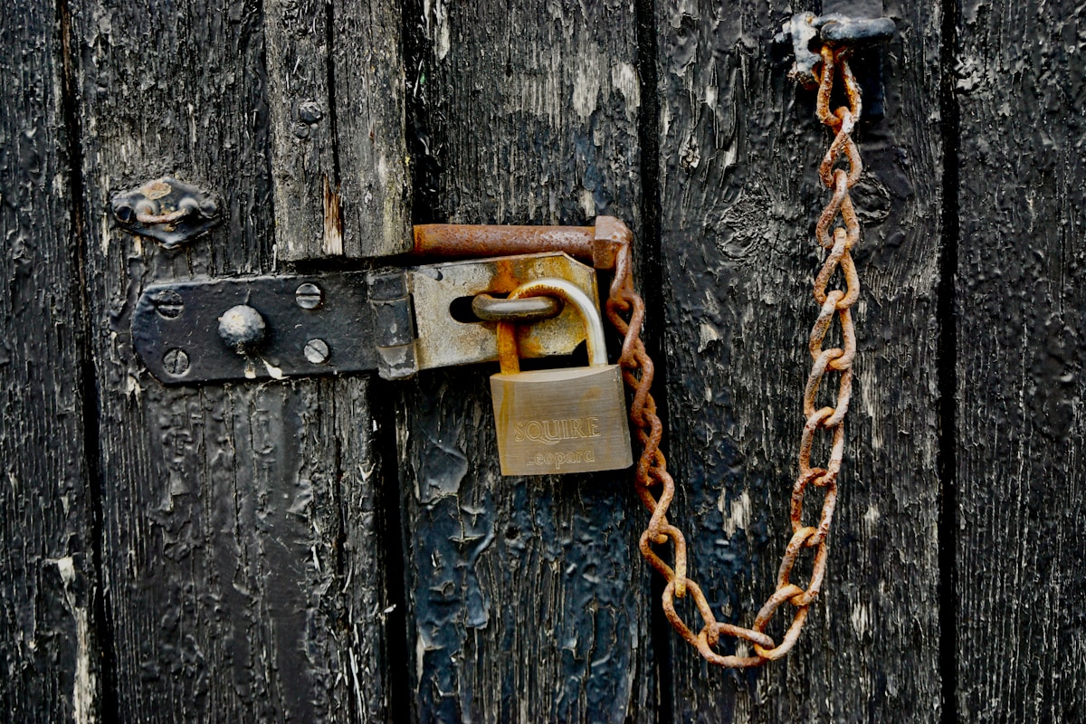 Verrou rouillé, chaîne en métal, porte en bois usagée.