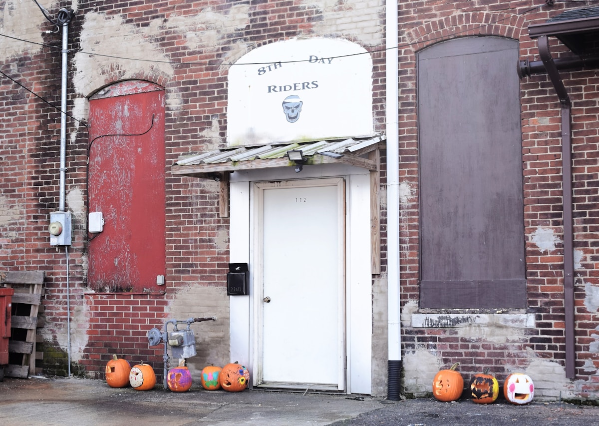 Entrée de bâtiment avec enseigne "8th Day Riders", citrouilles décorées pour Halloween.