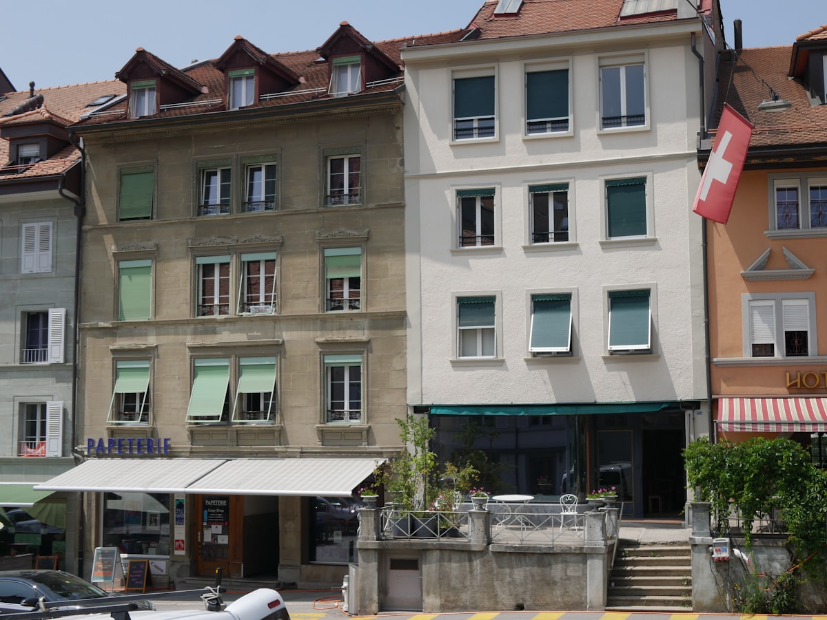 Bâtiments anciens avec fenêtres et balcons, terrasse de café, drapeau suisse.