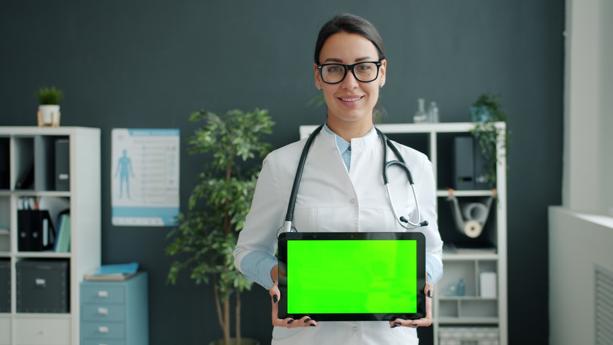 Médecin souriante tenant une tablette avec un écran vert.