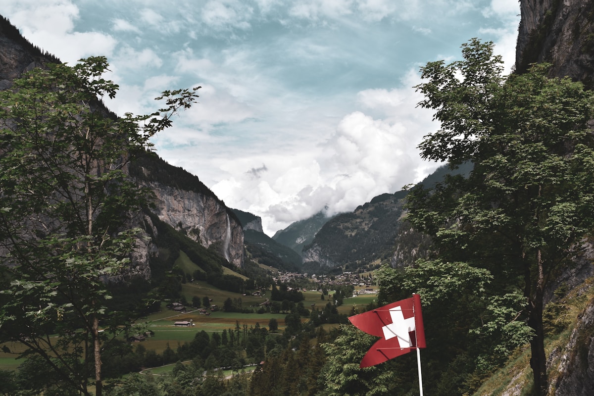 Paysage montagneux suisse avec drapeau national, vallée verdoyante et village.