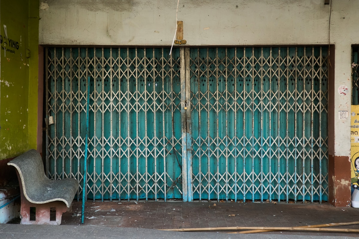 Porte métallique rétractable verte et bleu décrépie dans une ruelle.