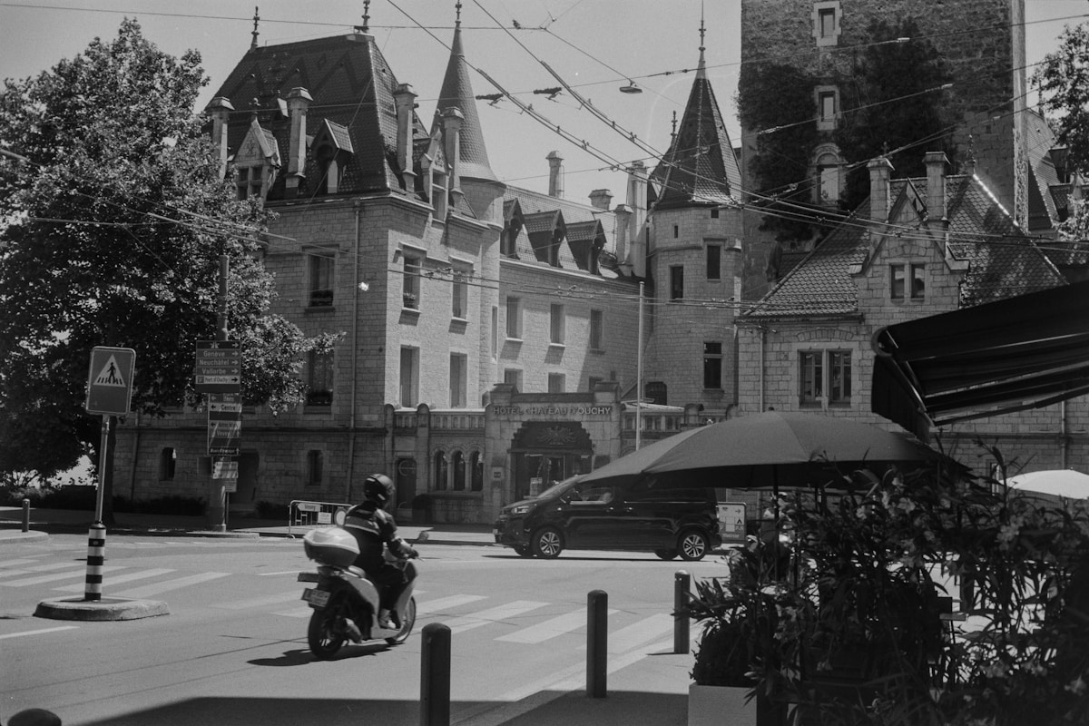 Bâtiments anciens, architecture gothique, scène de rue animée, moto, parasols, arbres.