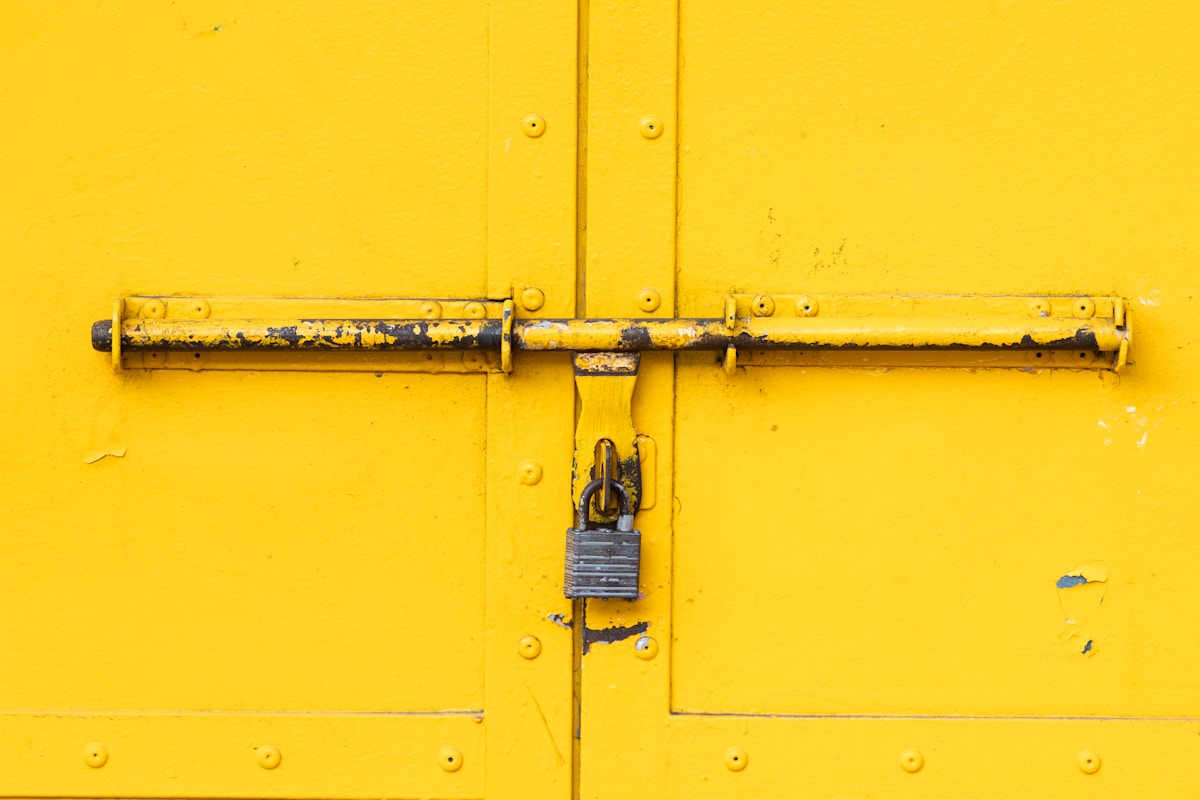 Porte jaune verrouillée avec un cadenas rouillé.