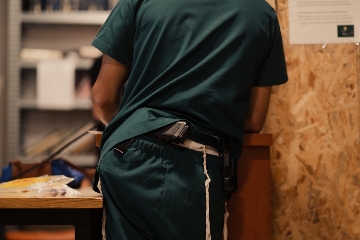 Personne portant un t-shirt vert foncé et un sac à dos dans un environnement intérieur.