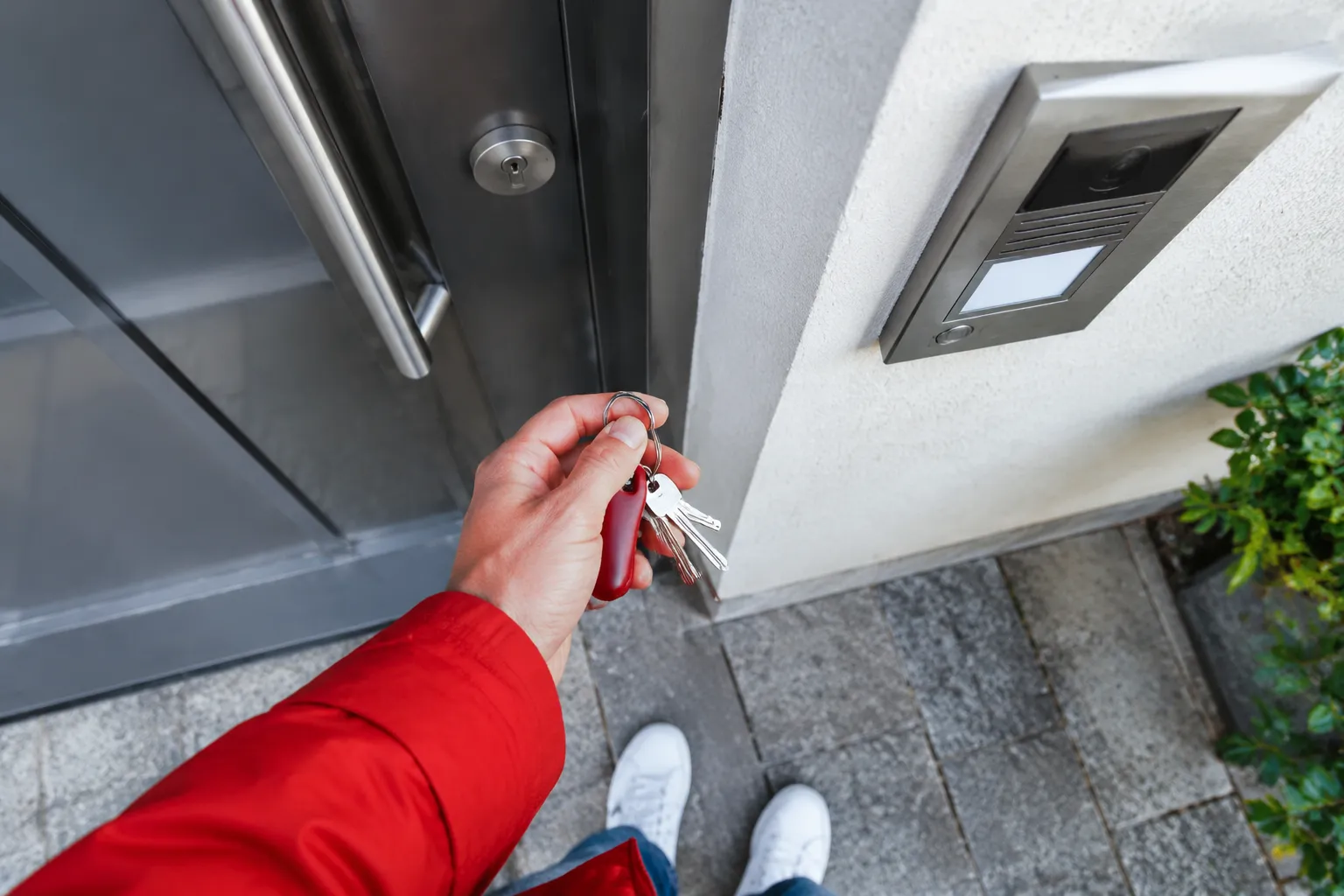 Main tenant des clés devant une porte avec interphone