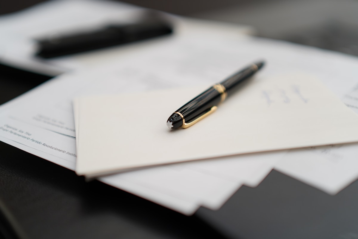 Stylo à bille noir sur papiers blancs sur un bureau sombre.