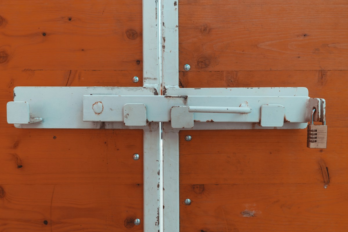 Verrou métallique blanc fixé sur porte en bois, cadenas.