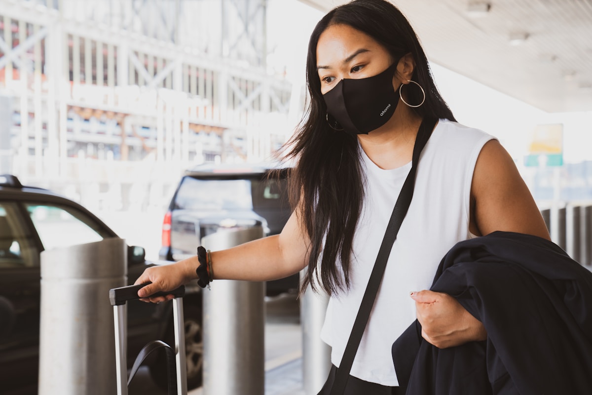 Femme asiatique portant un masque dans un aéroport, avec une valise.