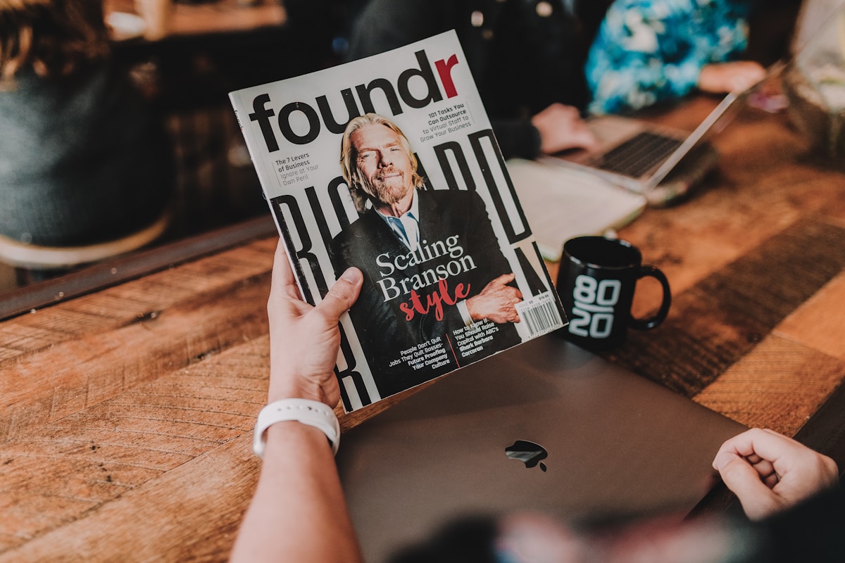 Magazine Foundr avec Richard Branson en couverture, ordinateur portable et tasse sur une table en bois.