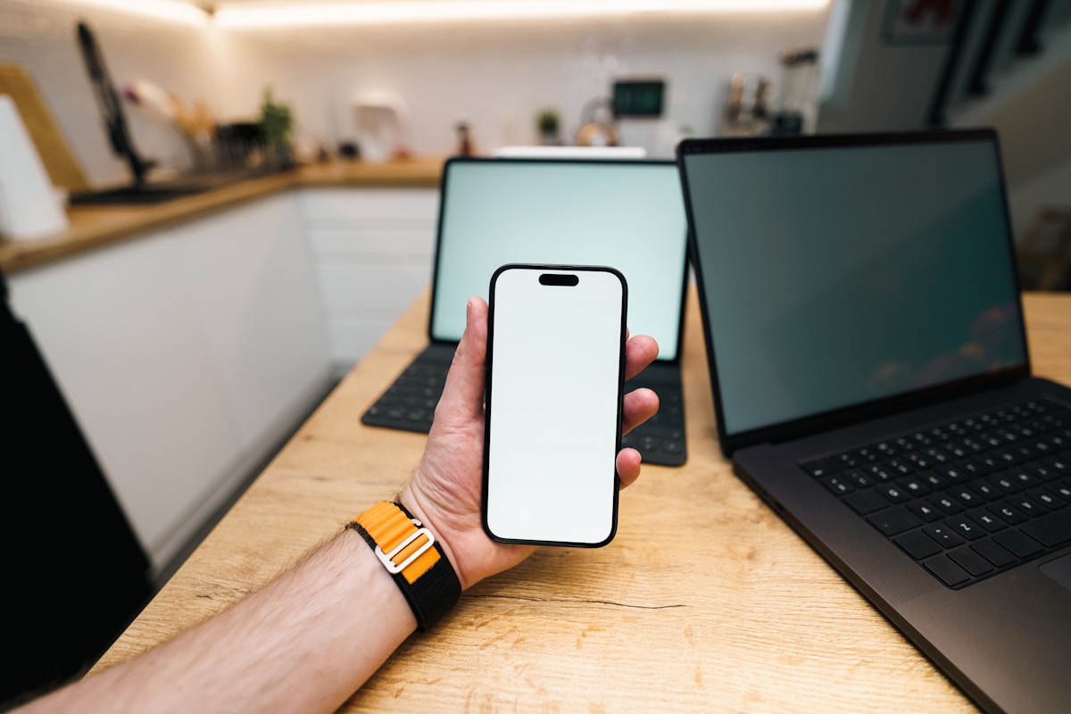 Téléphone portable avec écran blanc tenu dans une main près d'un ordinateur portable.