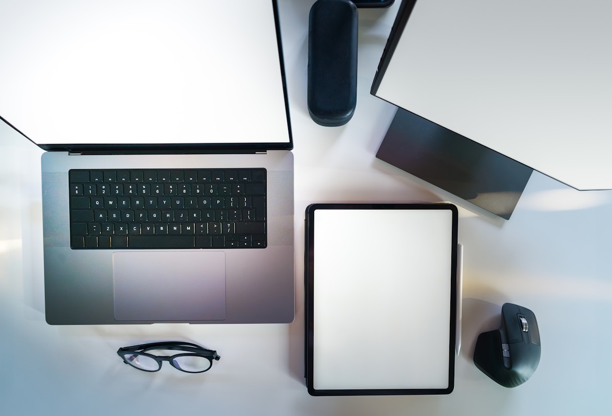 Bureau de travail avec ordinateur portable, tablette, souris et lunettes.