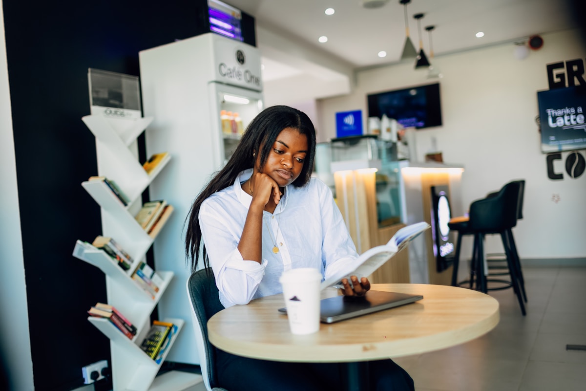 Femme afro-américaine assise, lisant un livre dans un café.