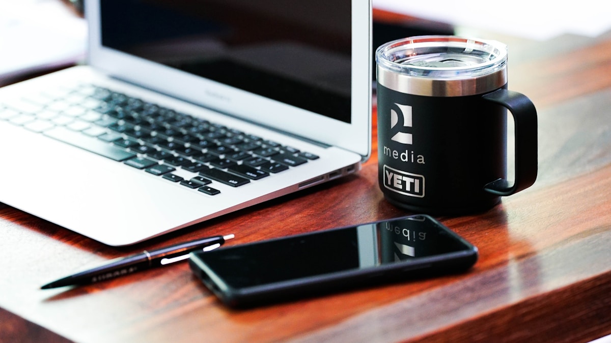 Bureau de travail avec ordinateur portable, tasse Yeti et téléphone portable.