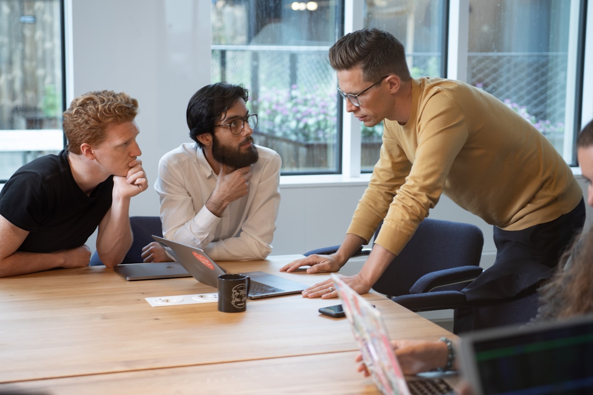 Trois hommes en discussion autour d'un ordinateur portable dans un bureau moderne.