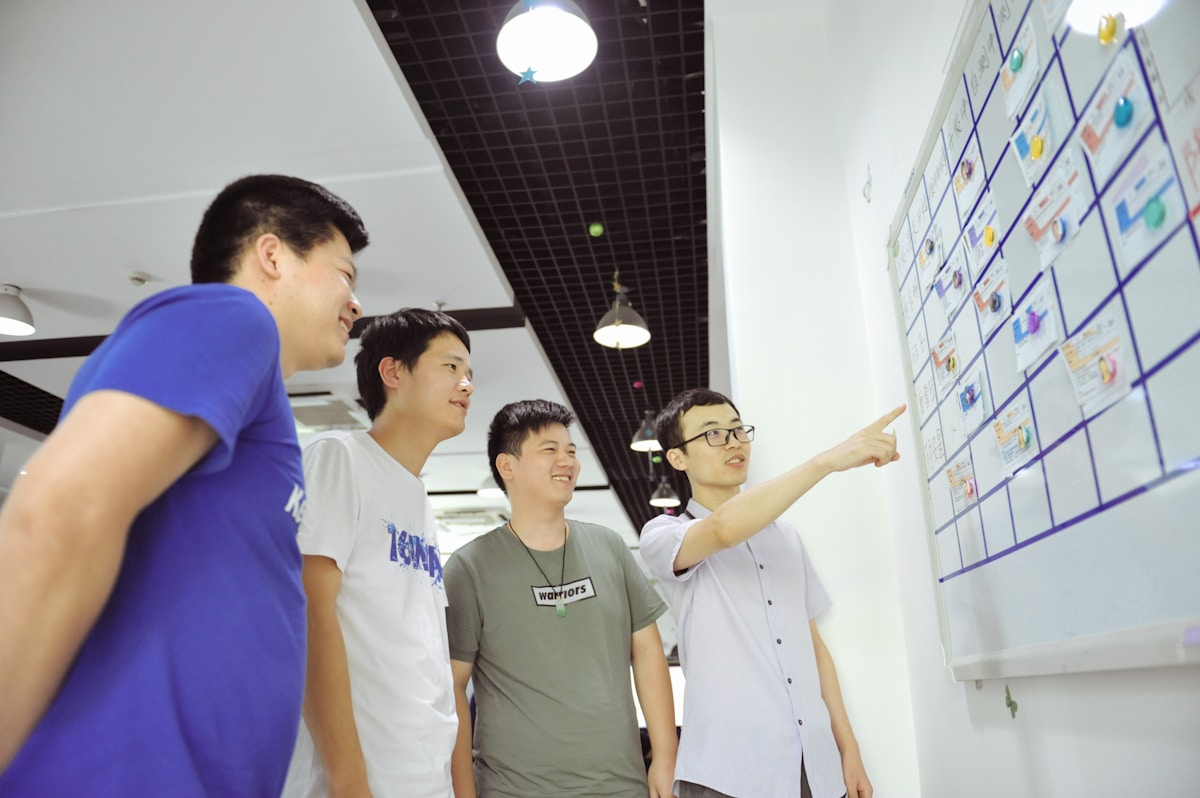 Groupe d'étudiants asiatiques discutant et travaillant ensemble sur un tableau blanc.
