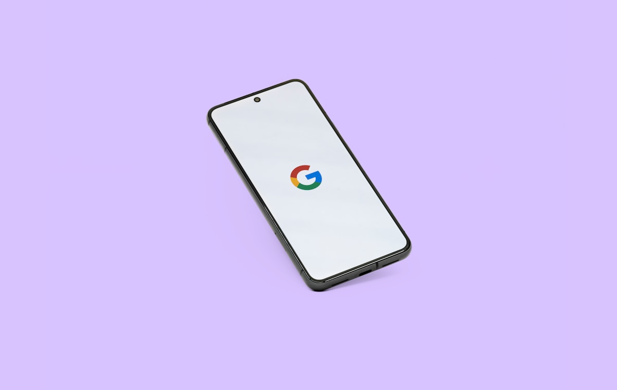 Smartphone noir avec logo Google sur écran blanc sur fond violet.