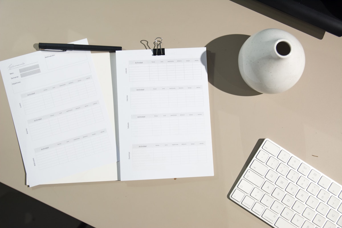 Papiers, stylo, clavier d'ordinateur et vase sur un bureau.