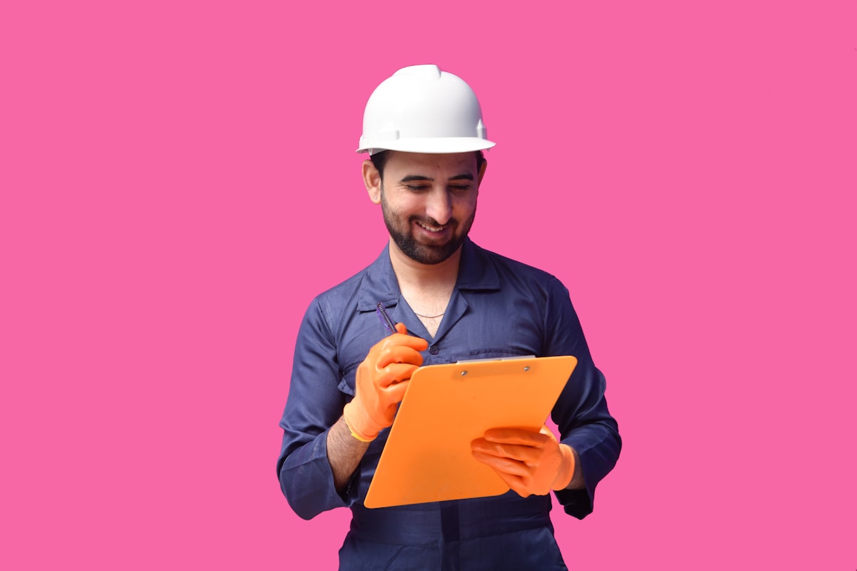 Ouvrier du bâtiment en uniforme tenant un presse-papiers orange.