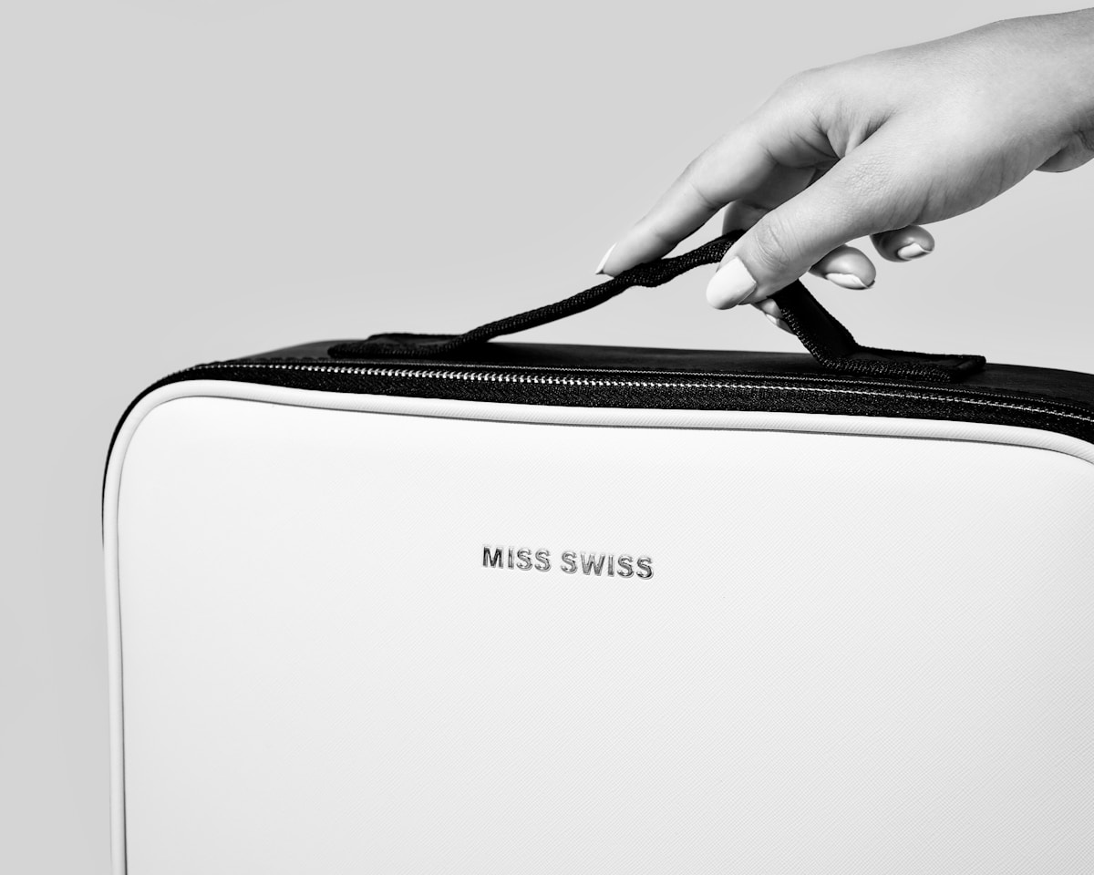 Valise blanche avec fermeture éclair noire et inscription "Miss Swiss".