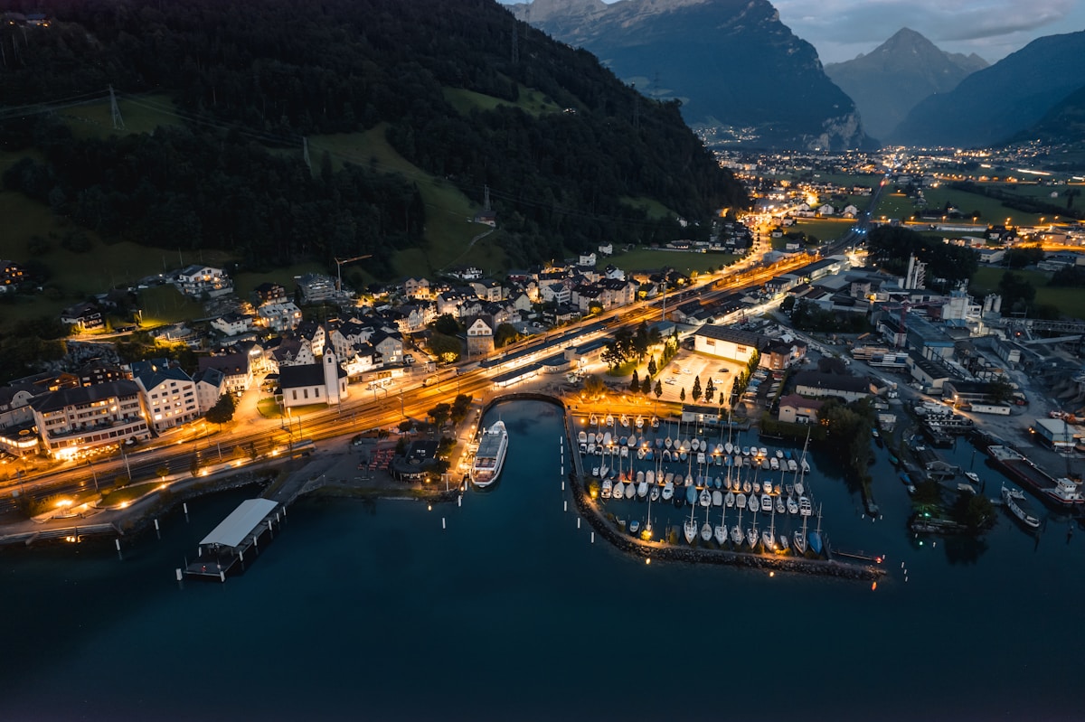 Ville de montagne illuminée la nuit, port de plaisance, paysage alpin majestueux.