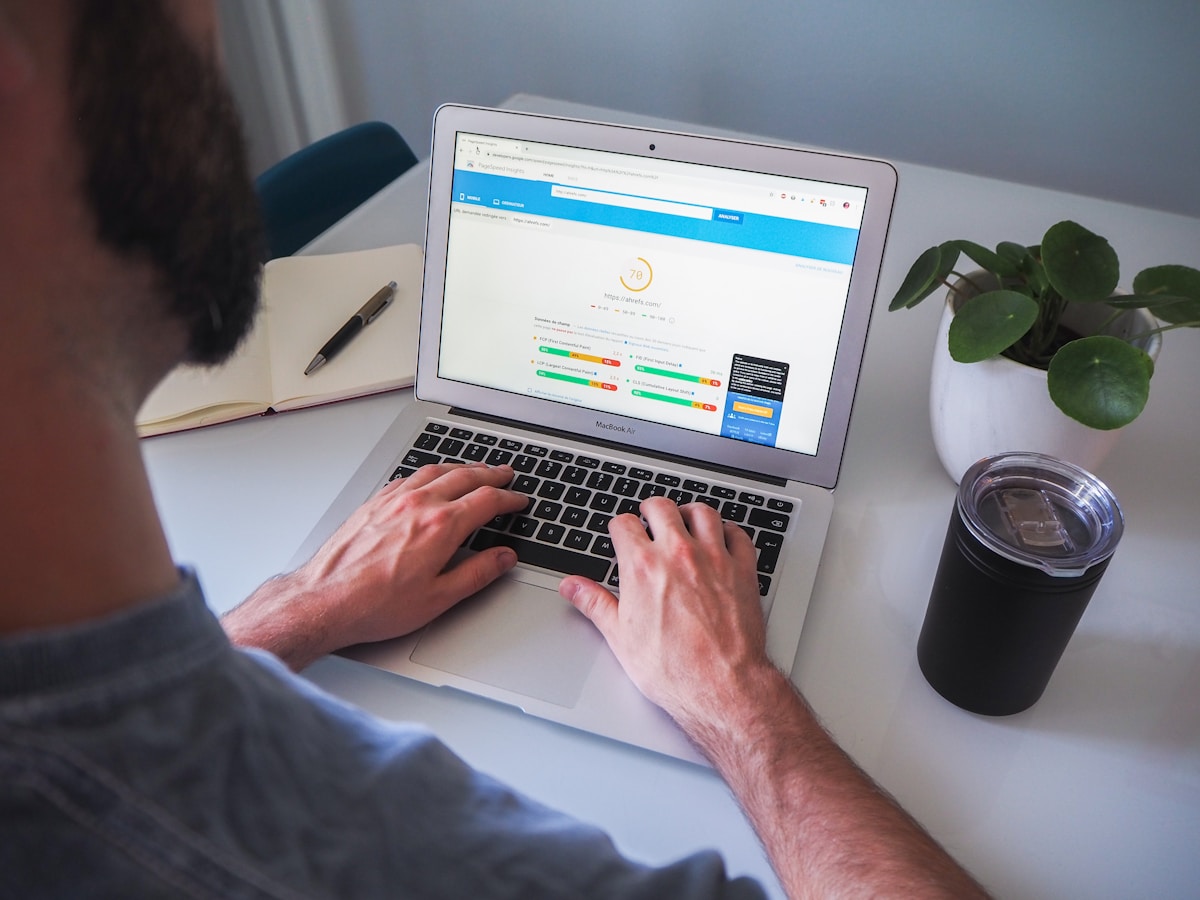 Personne utilisant un ordinateur portable avec un site web affiché à l'écran, sur un bureau avec une plante et une tasse.
